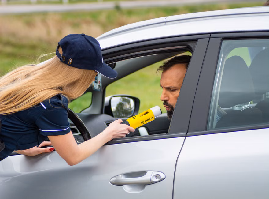 Police officer using breathalyzer to test driver's alcohol level outside car.