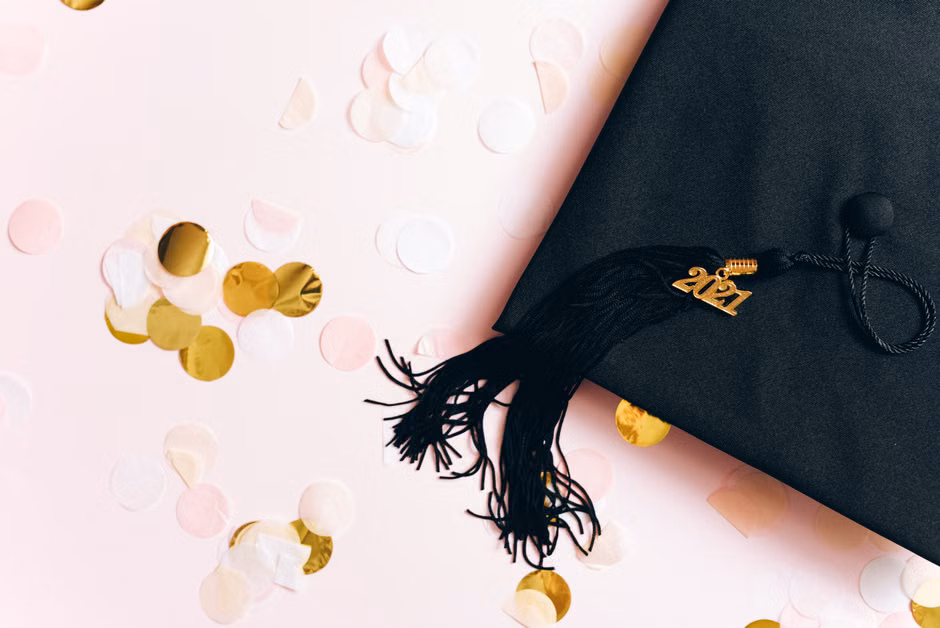 A graduation cap with a 2021 charm surrounded by festive confetti on a pastel background.