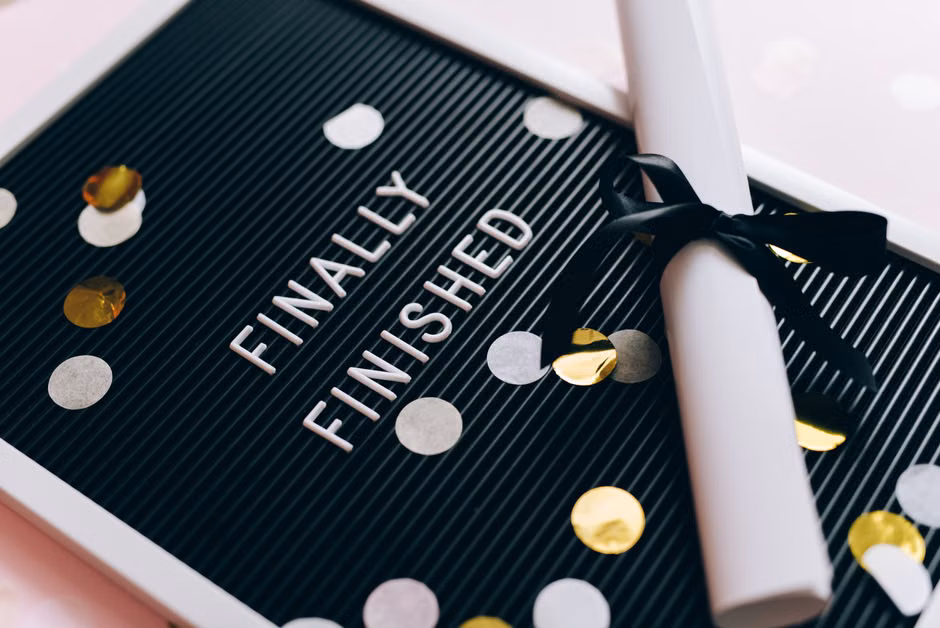 Close-up of a graduation diploma and letter board with 'Finally Finished,' surrounded by confetti.