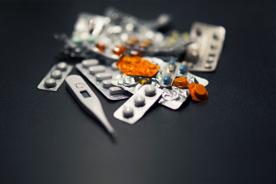 Close-up of various pills and a digital thermometer against a dark background.